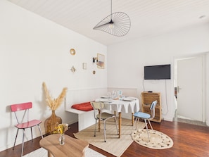 A dining area with a round table, chairs, a hanging light fixture, and a television mounted on the wall. - House for 5 with garden, close to the beach (Saint-Gilles-Croix-de-Vie)