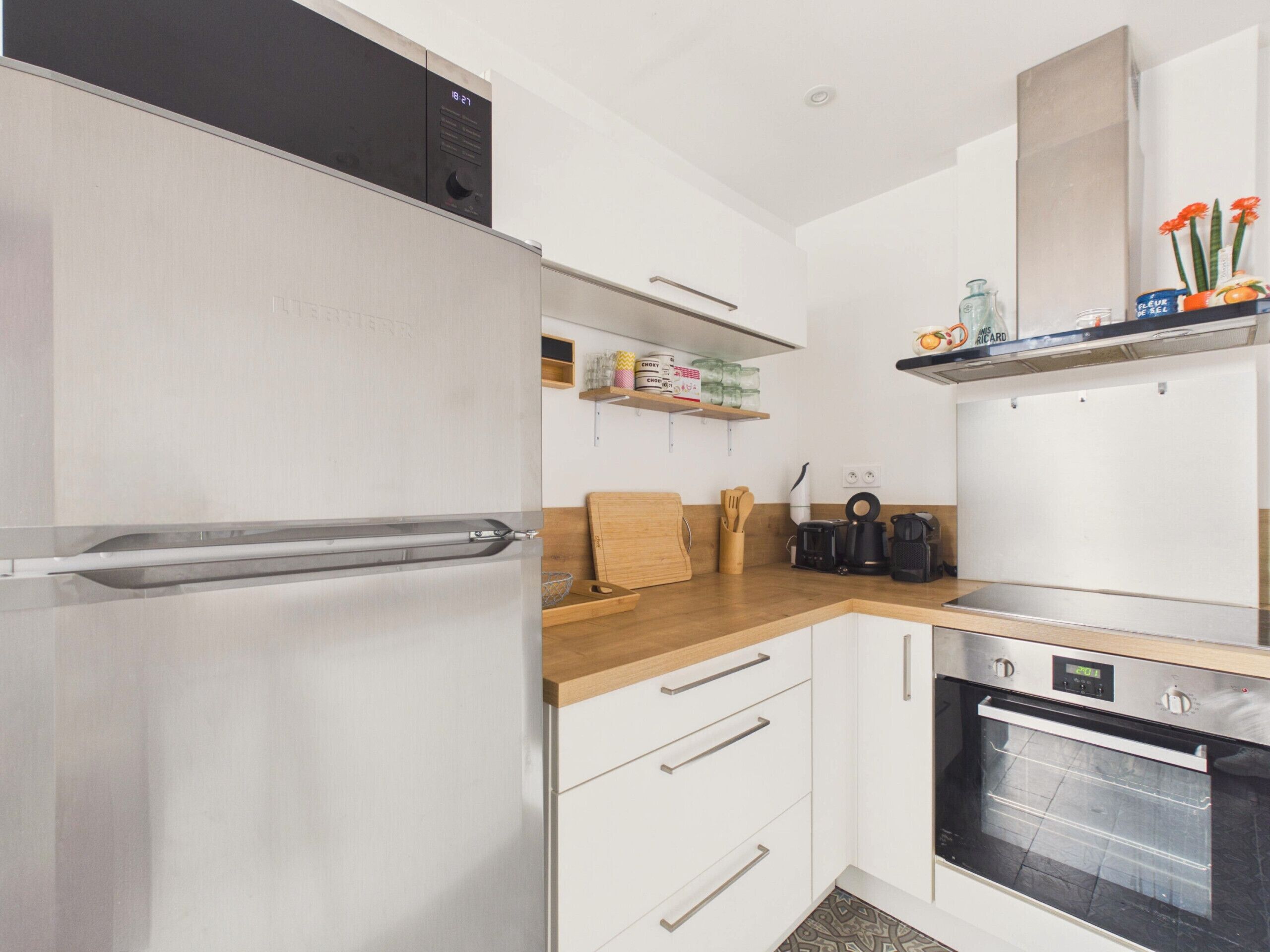 Una cucina compatta con frigorifero in acciaio inossidabile, forno integrato e piano di lavoro in legno.