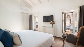 A hotel room with a bed, a TV, a glass table with a vase of flowers, and a view of an outdoor area. - Donna Angelina Arena View (Verona)