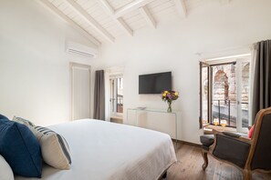 Ein Hotelzimmer mit Bett, Fernseher, Glastisch mit Blumenvase und Blick auf einen Außenbereich.