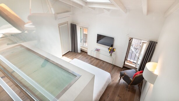 A modern interior with a glass balcony, a flat-screen TV, and a small table with flowers. - Donna Angelina Arena View (Verona)