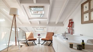 A modern bathroom with a skylight, two chairs, a round table, and a bathtub. - Donna Angelina Arena View (Verona)
