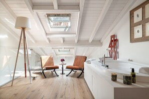 A modern bathroom with a skylight, two chairs, a round table, and a bathtub. - Donna Angelina Arena View (Verona)