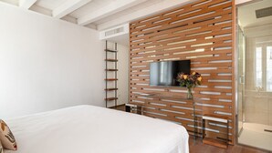 A modern bedroom with a bed, a TV mounted on a wooden panel wall, a glass table, and a shower area. - Conte Manfredo with Balcony (Verona)