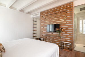A modern bedroom with a bed, a TV mounted on a wooden panel wall, a glass table, and a shower area. - Conte Manfredo with Balcony (Verona)