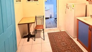 A small kitchen with a table, chair, and a refrigerator. There is a door with a number on it and a rug on the floor. - walkabout apart (fatih)