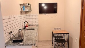 A compact kitchen with a TV mounted above the counter, a small dining table with chairs, and a white cabinet. - walkabout apart (fatih)