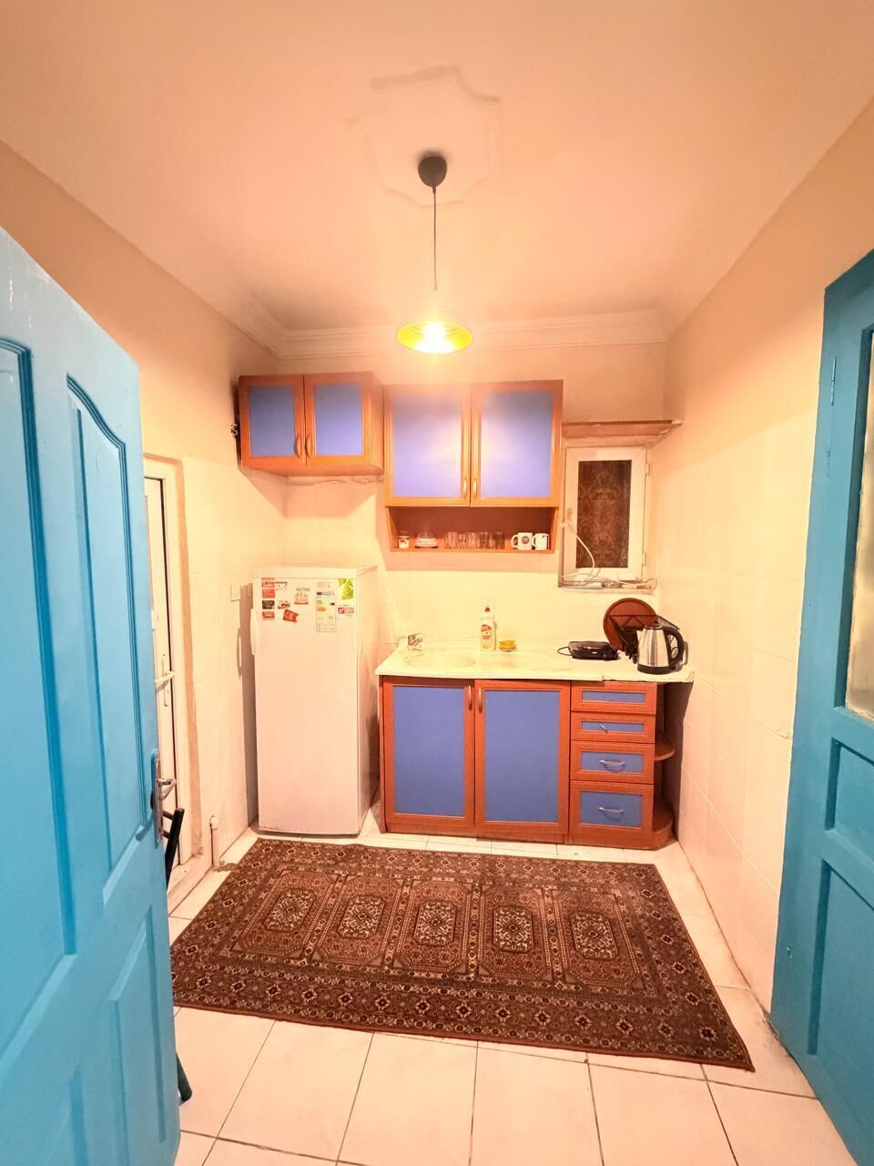 Uma cozinha compacta com geladeira, armários, chaleira e uma janela.