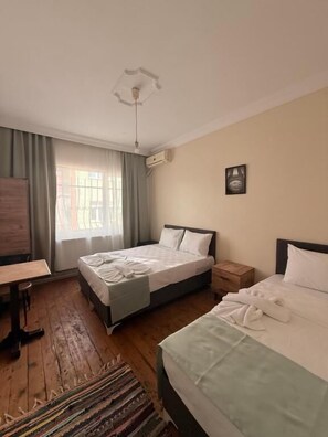 Een slaapkamer met twee bedden, een houten vloer, een plafondlamp, een raam met gordijnen en een aan de muur bevestigde airconditioner.