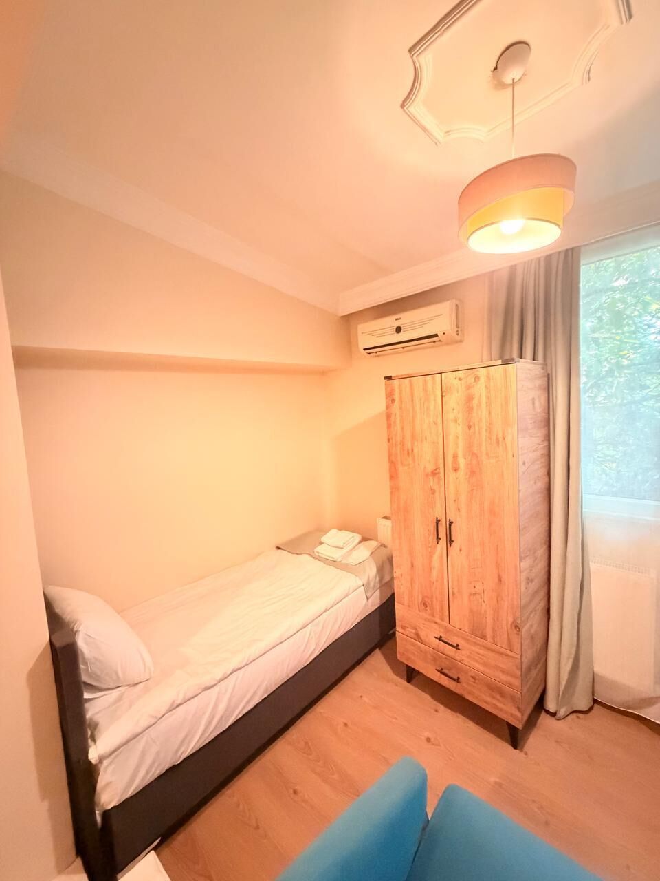 A bedroom with a single bed, a wardrobe, and a ceiling light fixture.