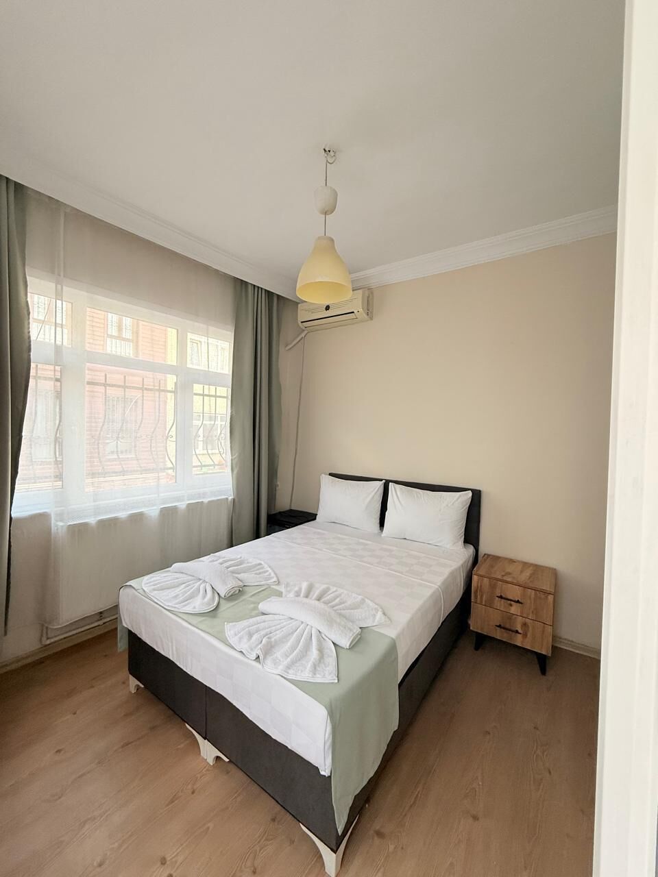 Un dormitorio con cama, mesita de noche, lámpara colgante y ventana con cortinas.