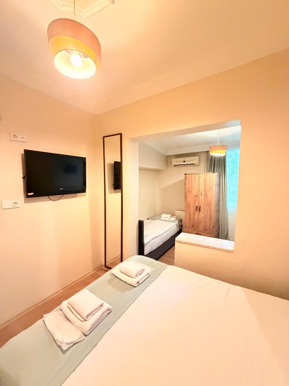 Une chambre d’hôtel comprenant un lit, un téléviseur à écran plat fixé au mur, une armoire en bois et une fenêtre avec des rideaux.