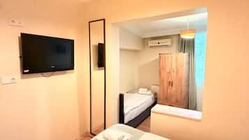 Une chambre d’hôtel comprenant un lit, un téléviseur à écran plat fixé au mur, une armoire en bois et une fenêtre avec des rideaux.