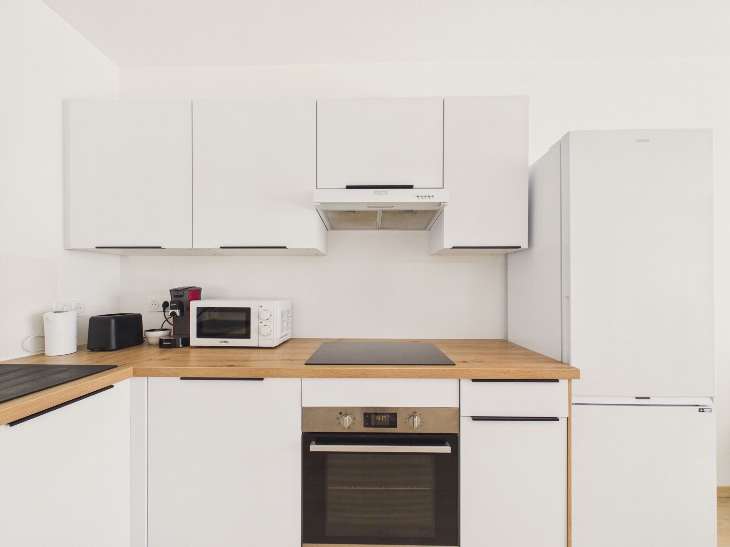 A modern kitchen with white cabinets, a microwave, a toaster, a kettle, and a refrigerator.