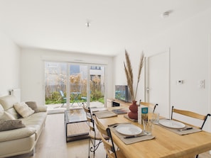 Ein modernes Wohnzimmer mit Sofa, Esstisch, Stühlen und Gartenblick durch Glastüren.