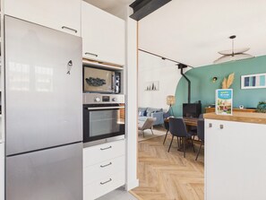 A modern kitchen with a built-in oven, microwave, and refrigerator. There is a dining area with a wooden table and chairs. - Near beach, house for 10 with garden (Erquy)