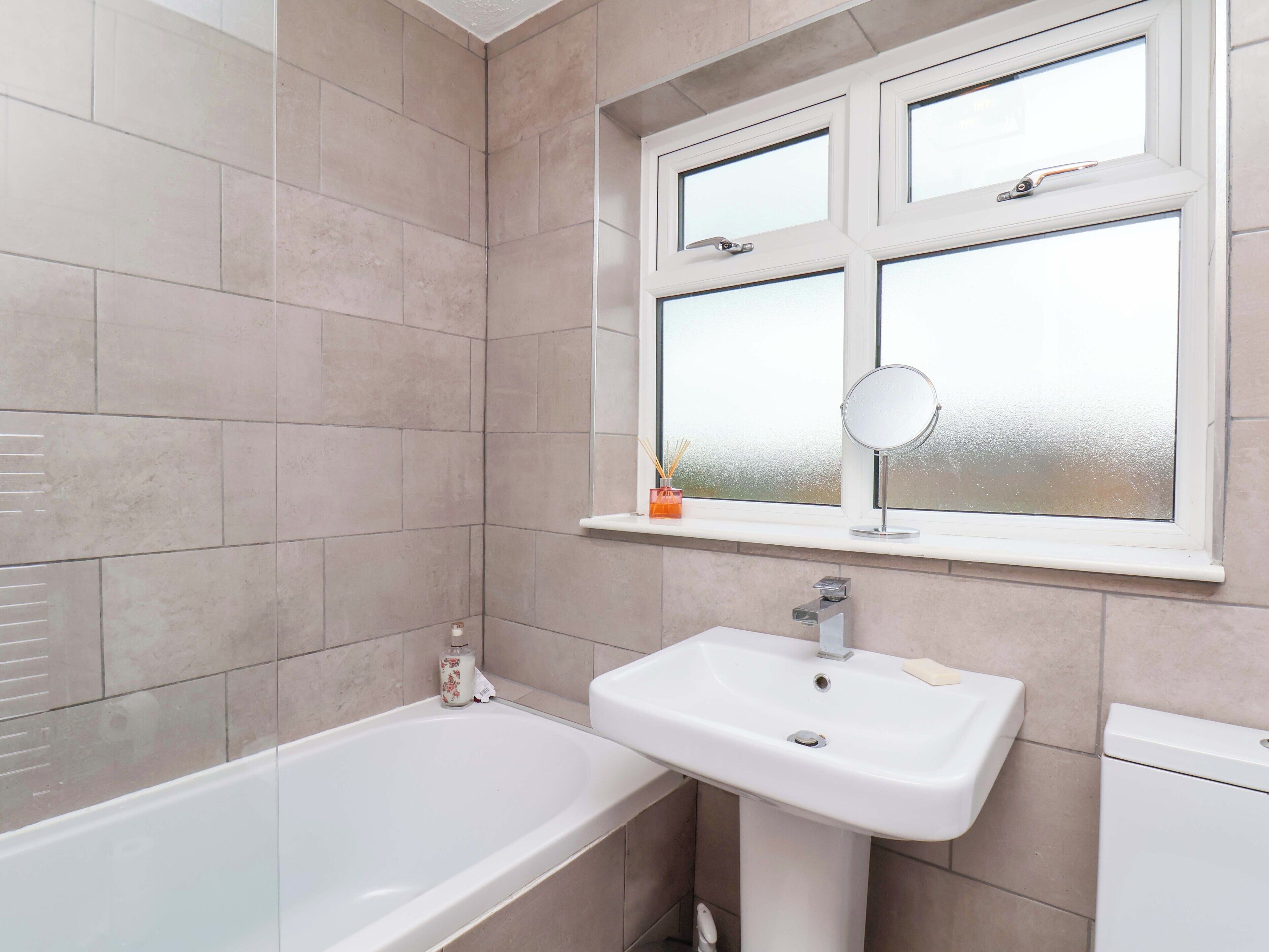 Un baño con bañera, lavamanos y ventana con espejo.