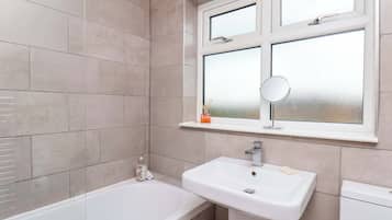 Un baño con bañera, lavamanos y ventana con espejo.