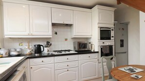 Una cocina con armarios blancos, microondas, horno, refrigerador, mesa de madera y lavadora.