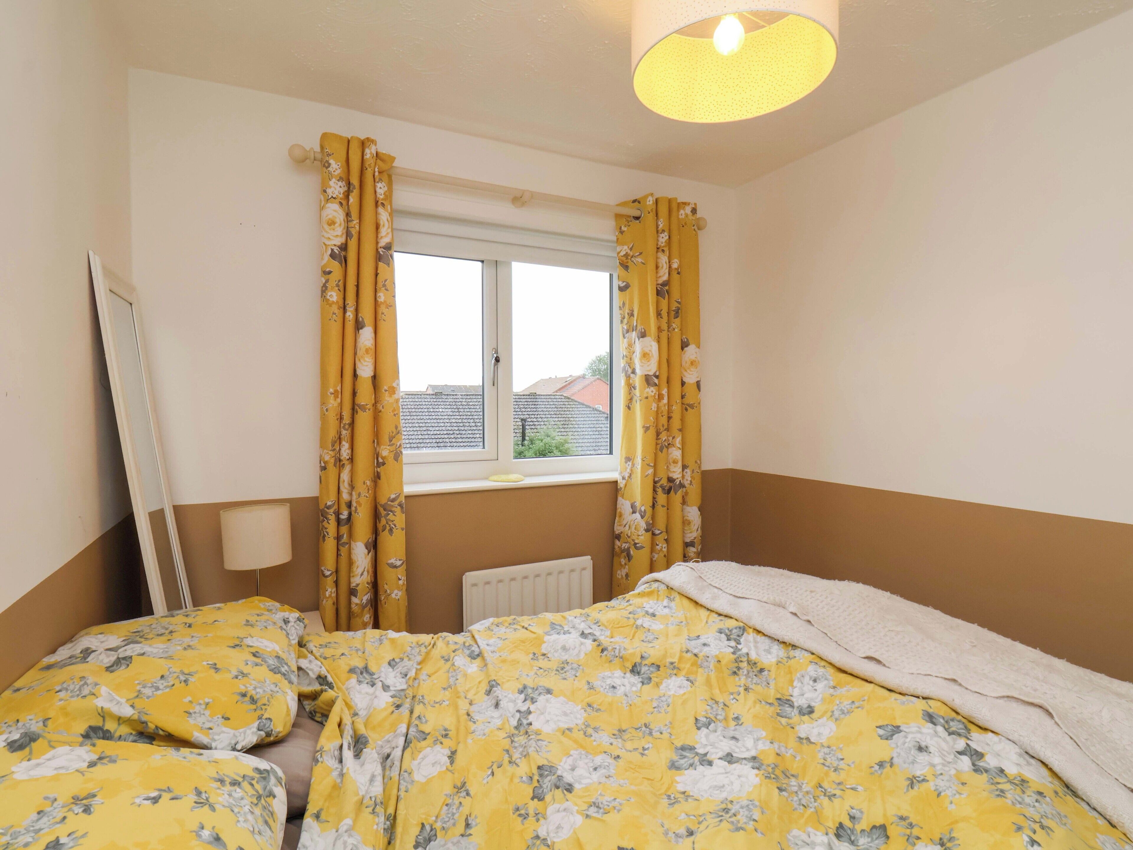 A bedroom with a bed, a radiator, and a window with curtains.