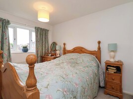 Un dormitorio con una cama de madera, una mesita de noche con lámpara, un aparador y una ventana con cortinas.