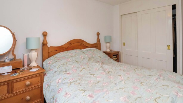 Un dormitorio con una cama de madera, una mesita de noche con lámpara, un aparador y un espejo.