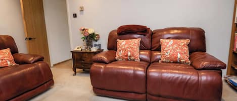 A living room with two brown leather recliners, a wooden side table with a vase of flowers, and a bookshelf.