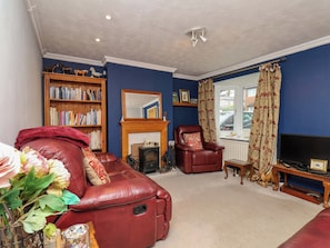 A living room with a red leather sofa, a fireplace, a bookshelf, and a television. - 7 Crestbrooke (Northallerton)