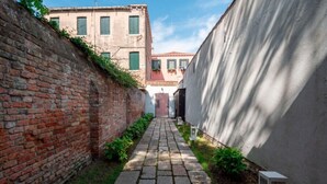 Un callejón estrecho con un muro de ladrillo a un lado y un muro blanco al otro, que conduce a un edificio con tejado rojo.