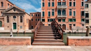 Un puente histórico con barandilla de madera que conduce a un canal flanqueado por edificios.