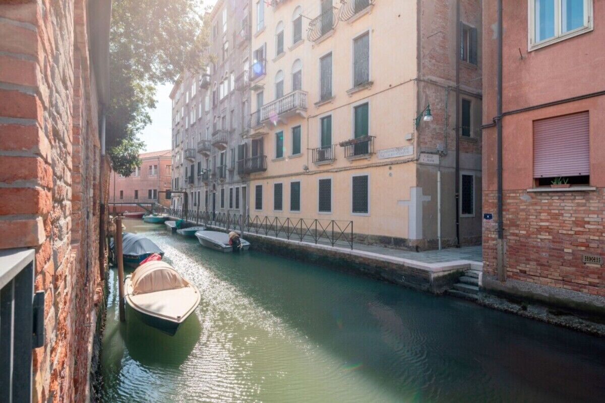 A narrow canal with boats, a brick building, and a row of multi-story buildings with balconies.