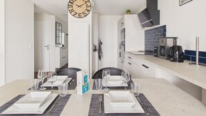 Una cocina moderna con un reloj de pared grande, una mesa de comedor para cuatro personas y una cafetera.