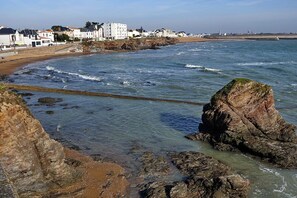 A coastal view with rocky shoreline, clear water, and buildings in the background. - Sea-view balcony & beach access - Sleeps 4 (Saint-Hilaire-de-Riez)