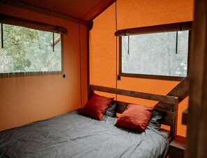 Ein Einzelbett mit Holz Kopfteil, zwei Fenster mit Vorhängen und Blick auf Bäume.