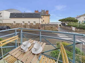 A balcony with a table set for tea, overlooking a street with buildings and a clear sky. - Sea view, near beach, lovely flat for 4 (Pléneuf-Val-André)