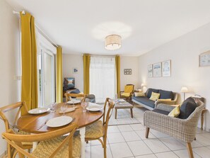 A dining area with a wooden table and chairs, a sofa, and a television in the background. - Sea view, near beach, lovely flat for 4 (Pléneuf-Val-André)