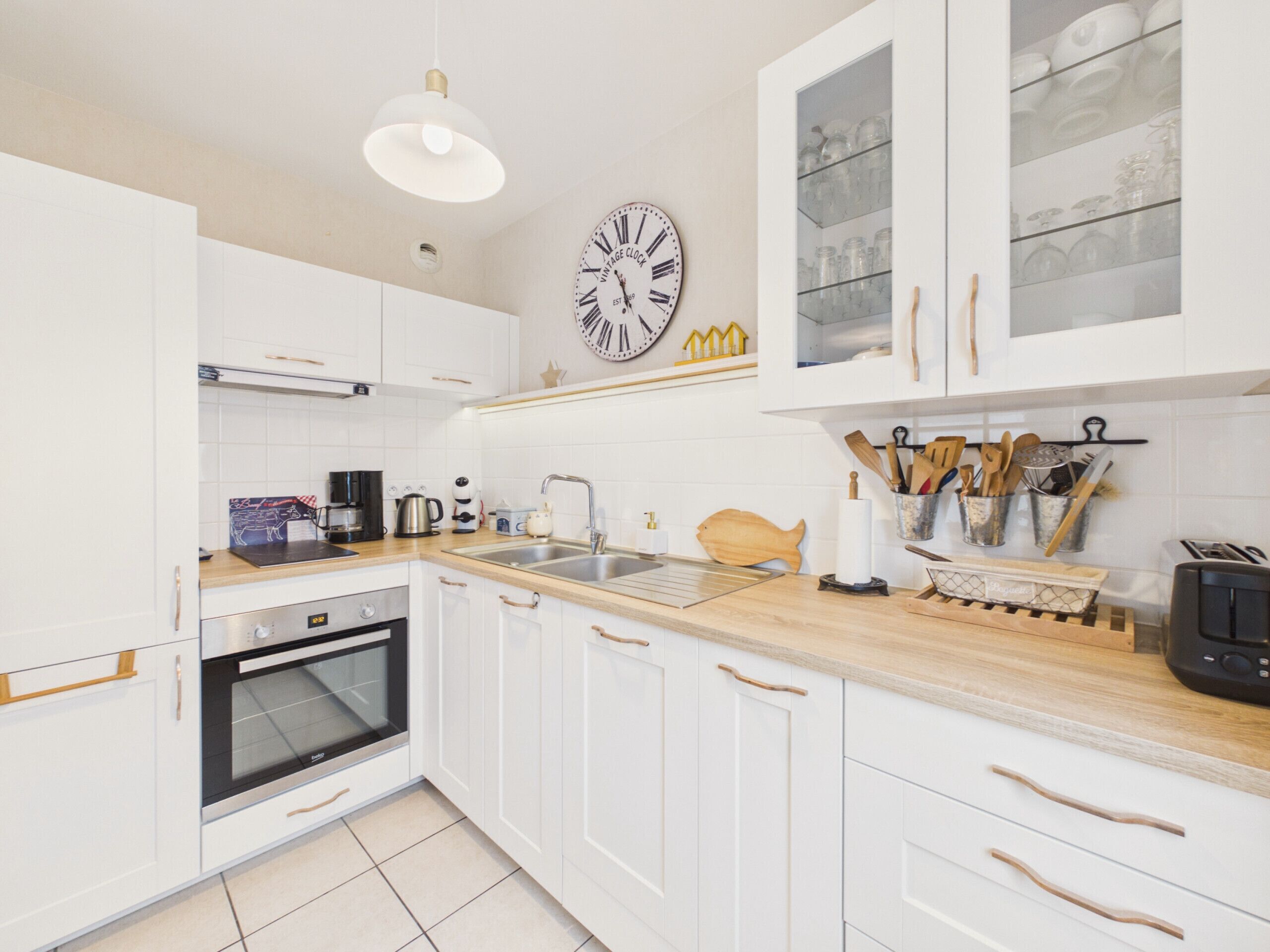 A kitchen with white cabinets, a wooden countertop, a built-in oven, a sink, and a wall-mounted clock.