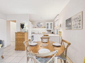 A dining area with a wooden table set for four, white cabinets, and a clock on the wall. - Sea view, near beach, lovely flat for 4 (Pléneuf-Val-André)