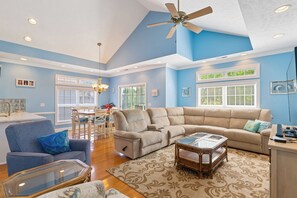 A living room with a sectional sofa, a glass coffee table, a ceiling fan, and a dining area with a table and chairs. - Beautiful private home with Updated appliances and community pool! (North Myrtle Beach)
