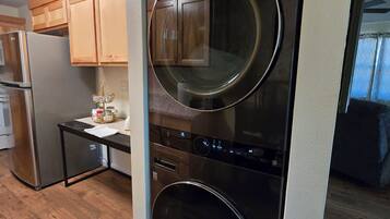 Een kleine keuken met een ingebouwde wasmachine en droger, houten kastjes en een roestvrijstalen koelkast.