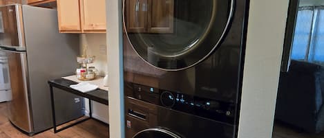 A compact kitchen with a built-in washer and dryer, wooden cabinets, and a stainless steel refrigerator.