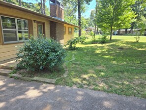 A residential house with a brick chimney, a front yard with grass, and a sidewalk leading to the door. - Trail-adjacent home with fenced yard. Pets Allowed! 
New A/C and heat. (Bella Vista)