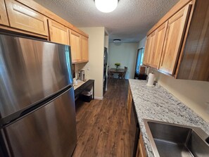 A kitchen with wooden cabinets, a stainless steel refrigerator, a granite countertop, and a wooden dining table with chairs. - Trail-adjacent home with fenced yard. Pets Allowed! 
New A/C and heat. (Bella Vista)