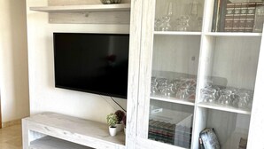 Ein Wohnzimmer mit Flachbildfernseher an der Wand, einer Holz-Unterhaltungsecke mit Glastüren und einem kleinen Topfpflanzen.