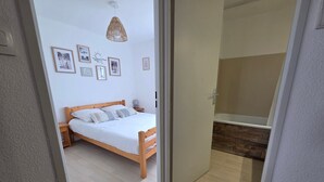 Une chambre à coucher avec un lit en bois, une table de chevet, une lampe fixée au mur et des tableaux encadrés.