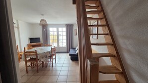 Une pièce comprenant une table à manger, des chaises, un téléviseur et un escalier.