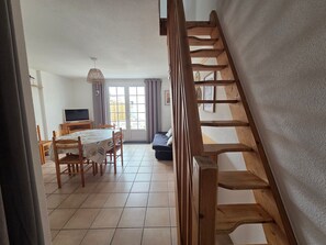 A room with a dining table, chairs, a TV, and a staircase. - Cozy cottage, garden, parking - 6 guests (La Tranche-sur-Mer)