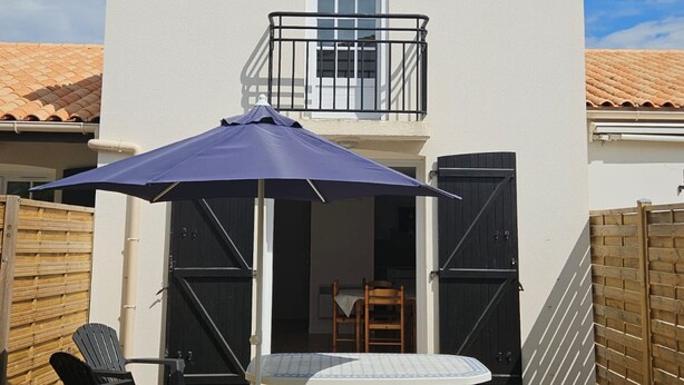 Un balcon avec une table et des chaises, un parasol bleu et une clôture en bois.