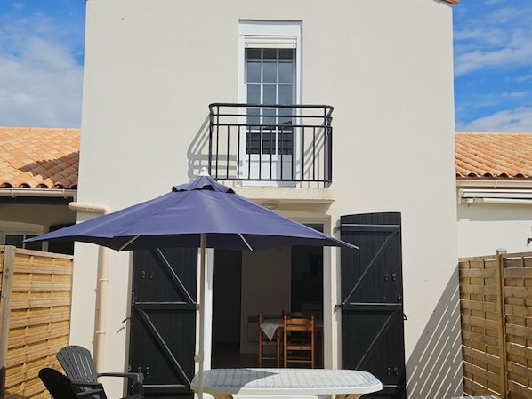 A balcony with a table and chairs, a blue umbrella, and a wooden fence. - Cozy cottage, garden, parking - 6 guests (La Tranche-sur-Mer)