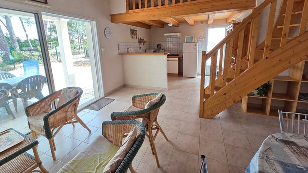 Amplia sala de estar con cocina, comedor y una escalera de madera.